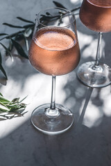 Rose wine in glasses on a table in the sun's rays, olive branches. Mediterranean, California wine, winery, summer vibes, close up