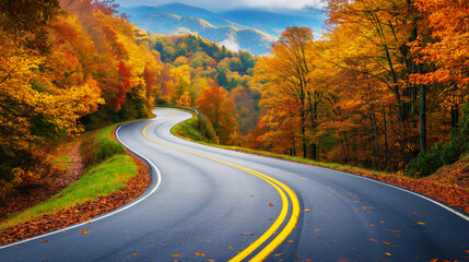 Fototapeta premium Scenic curved road through a forest with vibrant autumn foliage in yellow, orange, and red hues. Wet road and misty mountains in the background.