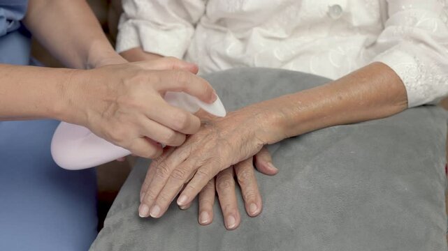 Female caregiver assisting massage and apply lotion on elderly hand for moistering dry skin
