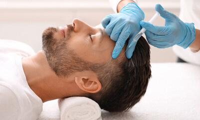 Side view of handsome middle aged man getting hair treatment at beauty salon. Man having mesotherapy session at aesthetic clinic, therapist hands in gloves making injection in scalp, closeup