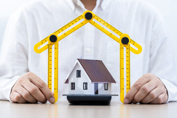 Businessman hand holding a folding ruler in the shape of the house on the desk in the office, Loan for real estate or construction industry a new house and renovation to estate in the future concept.