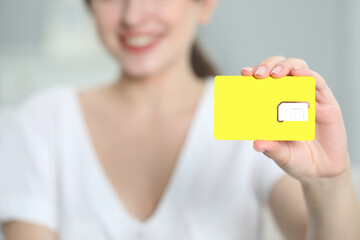 Woman holding SIM card at home, closeup