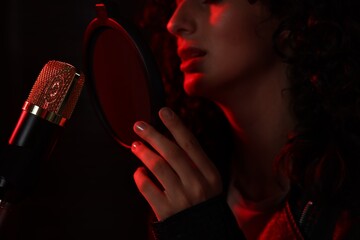 Woman singing into microphone in professional record studio with red light, closeup