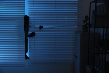 Thief looking out of blinds at night. Burglary