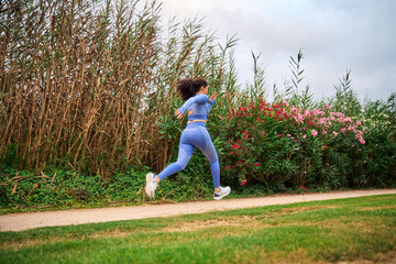 Woman running in blue activewear through a park on a cloudy day