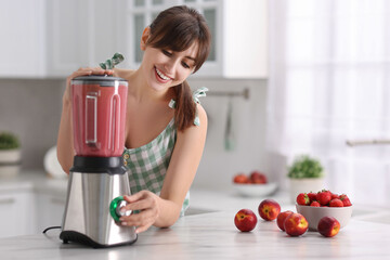 Young woman making delicious smoothie with blender at white marble table in kitchen