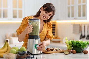 Young woman making delicious smoothie with blender at white marble table in kitchen