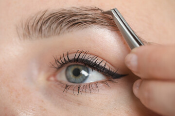 Beautician plucking young woman's eyebrow, closeup view