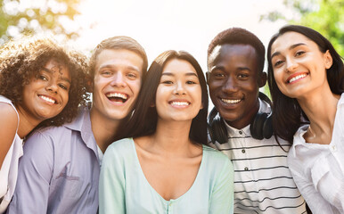 Portrait of cheerful interracial teen friends posing at camera outdoors, smiling and laughing, enjoying spending time together, closeup