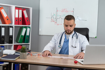 Male doctor in white coat and stethoscope work with report documents at office desk, medical clinic