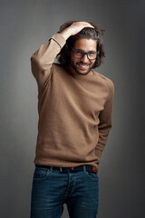 Naklejka premium Fashion, portrait and man in studio with smile for trendy clothes, casual outfit or denim jeans on gray background. Style, wardrobe and male model for designer glasses, winter jersey or confidence