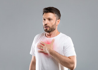 Breathing problem. Sick middle-aged man with chest pain touching inflammated zone and looking at copy space, grey studio background. Bearded man suffering from pneumonia or asthma. COVID-19 concept