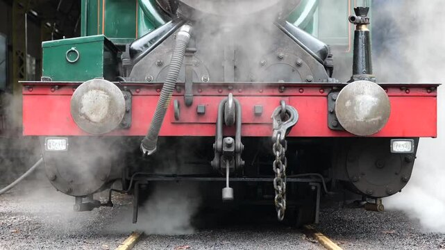 Front detail view of a small and old steam-powered locomotive. An old steam train at the station. Old, ancient steam-powered train ready to leave the station. Green and red colored ancient train.