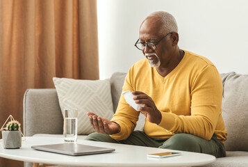 Mature Black Man Taking Medication Pill Putting Medicine On Hand Sitting Near Table With Laptop And...