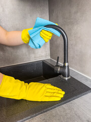 close up housewife in yellow gloves wiping a kitchen faucet with a sponge