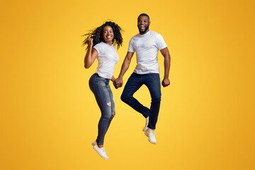 Cheerful Black Man And Woman Are Jumping In The Air, holding hands, copy space