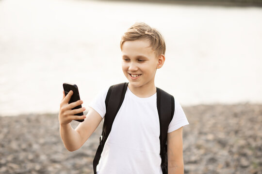 Teenager boy taking selfie with smartphone in park near a pond