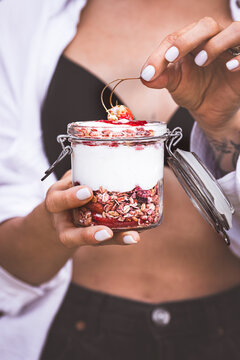Woman holding a jar of yogurt parfait with fruits and granola