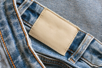 Fashion detailed background with empty copy space fror graphic design. Brown, blank leather label tag. Blue jeans denim texture with thread sew lines.