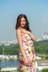 A young happy girl in a bright dress standing on a green grassy hillside on a sunny day enjoying...