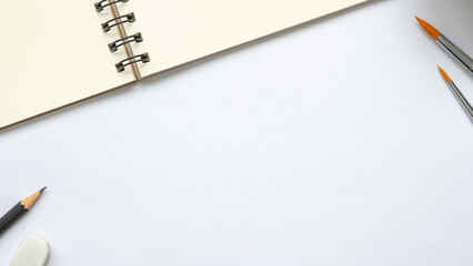 open blank spiral notebook with paintbrush, pencil and eraser on white background, Empty Space for your text, top view of workspace.