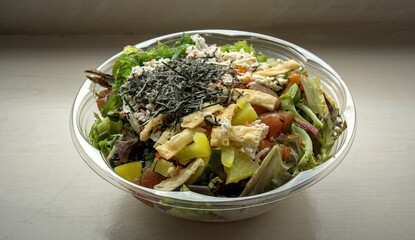 poke bowl hawaiian seafood dish in takeout container isolated on table (wonton crisps, nori, seaweed salad, kani crab, pickled daikon raddish, salmon, tuna, ponzu, shiitake mushrooms) sushi sashimi