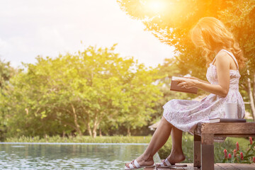 young woman in a vintage white dress sits on a poolside terrace reading the Bible alone to learn and understand God's teachings from the Bible she is meant to read. concept of belief and faith in God