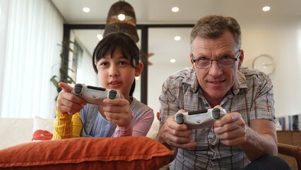 Grandfather and granddaughter together play console game, entertainment media. Old senior use technology communicate with new generation kid cross generation gap strengthen family bond. Divergence.