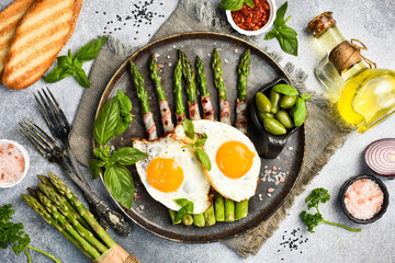 Useful nutritious breakfast. Plate with fried asparagus, bacon and fried eggs. Top view.