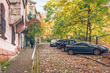 Lviv, Ukraine - November 2, 2023: A man walks up a cobblestone road, passing parked cars on the narrow Tsytadelna street in Lviv. Autumn vintage cityscape in the Old Town of Lviv