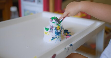 A young child engaged in painting with various Colorful Paints colors and paintbrush on a white table at home, showcasing creativity and early childhood development.