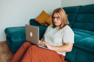 Upset sad, skeptical, serious woman in glasses working at the notebook near the sofa at home....