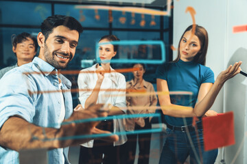 Professional businessman writing on glass wall at night office while coworker listening carefully. Group of business team working together,brainstorming, sharing marketing idea. Business plan.Tracery.