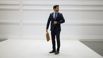 Fototapeta premium Professional business man standing with cool pose at white background. Manager holding bag while finding partner or looking around. Caucasian working man prepare himself for presentation. Exultant.