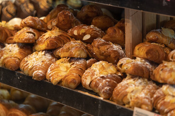 Close-up view of fresh baked brown puff almond croissants lying on shelf in bakery or cafe. Small business. Soft focus. Food background. Pastry theme.