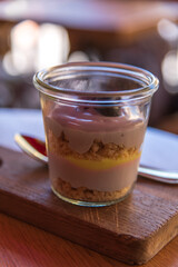 Close-up view of portion of trifle dessert in glass cup standing on wooden table in sidewalk cafe or street restaurant in a sunny summer day. Soft focus. Sweet food theme.