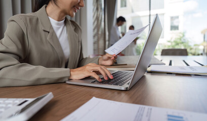 Fototapeta premium Businesswoman Analyzing Documents and Working on Laptop in Modern Office Environment