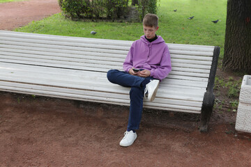 A boy sits on a bench with a phone.