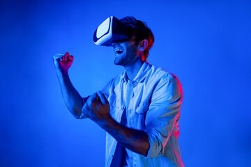 Happy excited man watching at sport competition at virtual world while wearing VR headset at neon...