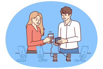 Woman buys new mobile phone in consultation with employee of digital gadget store. Man and girl are standing near showcase with smartphones connected by wire to counter, to avoid stealing phone