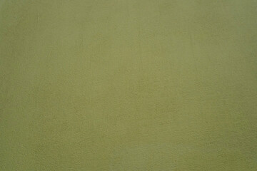 Olive paint on a concrete wall, plaster background. Rough textured stucco surface painted with brush, details in selective sharpness in the centre.