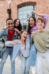 Vertical group of smiling teenagers posing happily for a portrait. Young people laughing and having fun looking at the camera. Guys giving piggyback to their female friends. Mates enjoying together