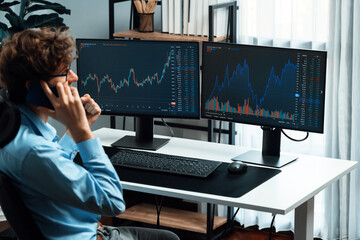 Young investor stock trader discussing on smartphone to broker, looking on dynamic financial exchange investment on screen at back side in current market graph in real time at modern office. Gusher.