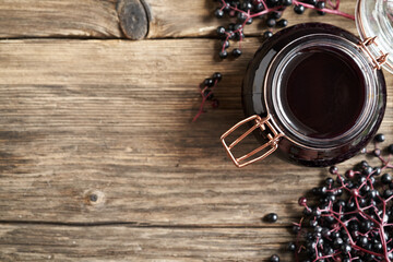 Homemade black elder syrup with fresh elderberries on wooden background with copy space