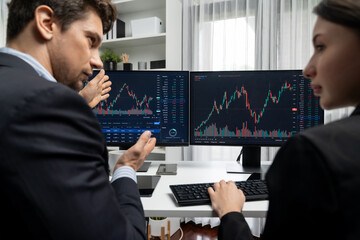 Two business traders discussing on dynamic stock market in currency rate investment trading on two pc screens with compare real time graph on risk or profit point of data at modern office. Postulate.