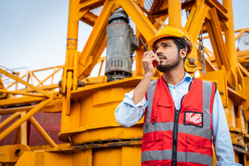A man in a yellow hard hat and red vest is talking on a walkie talkie