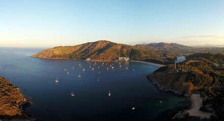 Aerial view of a bay with yachts anchored, surrounded by lush hills and clear skies at sunset