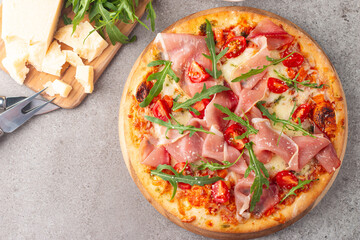 Pizza with prosciutto, ham, arugula, spinach, tomatoes, pesto, cheese and parmesan. Italian cuisine. 