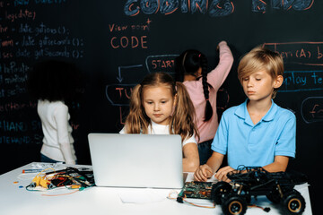 Smart girl in white bib learning about coding robotics technology using laptop in the STEM class. Schoolboy in blue shirt try to educate motherboard while smart schoolgirls reading code. Erudition.