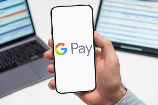 PRAGUE, CZECHIA - JULY, 2024: Google pay logo on the screen of smartphone in mans hand and laptop on the background 